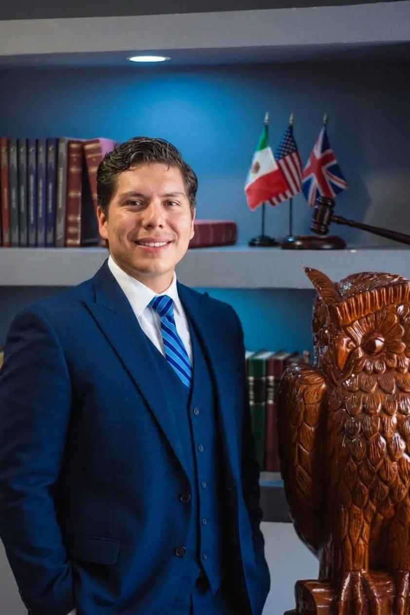 Modesto Flores González, socio director, con traje azul marino frente a un librero con banderas de México, Estados Unidos y Reino Unido